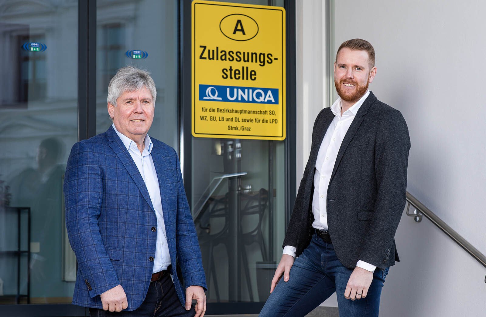 Zwei Mitarbeiter der Generalagentur Reichard vor dem Schild der KFZ Zulassungsstelle
